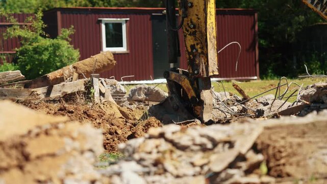 Heavy machinery dismantling an old building foundation at a construction site, with the excavator bucket crushing concrete and rebar during demolition work for redevelopment projects