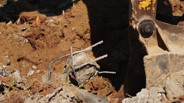Heavy machinery at a construction site digging a trench and removing a piece of concrete foundation with reinforced steel bars, preparing the land for building during daytime earthwork