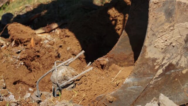 Heavy machinery at a construction site digging up earth and concrete rubble with rebar. Close up view of the excavator bucket working on a demolition and excavation project during a sunny day