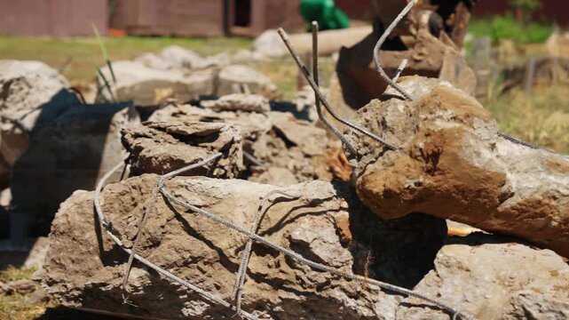 Heavy machinery bucket pushing and moving broken reinforced concrete blocks with rebar at a construction site during demolition work, showing a close up of the debris on the ground