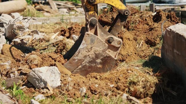 Heavy machinery's excavator bucket digging into the ground during demolition work on a construction site. The powerful metal scoop moves earth, rocks, and debris while preparing the foundation