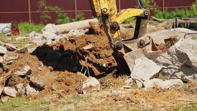 Heavy machinery at work on a construction site, with an excavator bucket breaking up concrete and digging soil during demolition, showcasing industrial power and site preparation