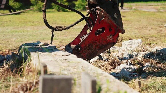 Close-up of a hydraulic breaker resting on an old concrete foundation before demolition, showing heavy construction equipment, structural removal and residential site preparation.