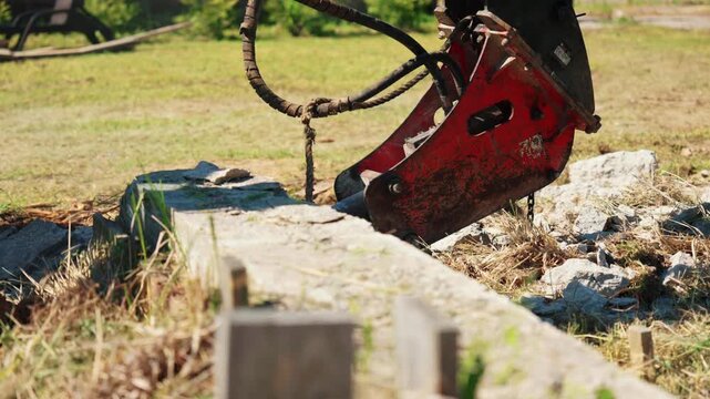 Heavy duty hydraulic hammer attached to an excavator arm breaking and destroying a reinforced concrete beam at a construction site, sending dust and debris flying with each powerful impact