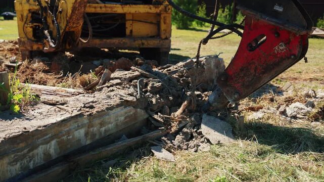 Powerful hydraulic breaker attachment on an excavator demolishing a large reinforced concrete slab during site preparation work, breaking it into smaller pieces of rubble and debris