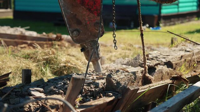 Powerful hydraulic breaker destroying an old concrete foundation at a construction site. The industrial jackhammer is crushing and smashing the reinforced concrete into rubble and dust