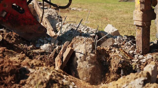 Close-up of a hydraulic breaker crushing a broken concrete foundation beside twisted reinforcing steel during residential demolition, showing structural removal, heavy equipment and site cleanup.