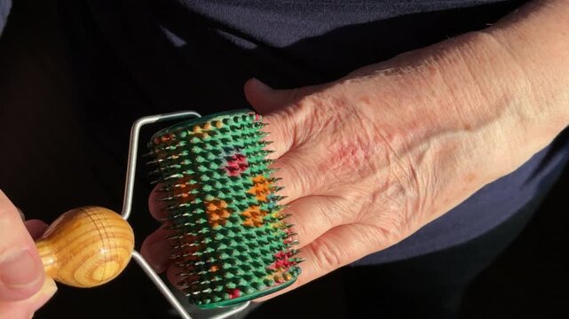 Close-up woman hands rolling green needle roller, wooden handle guiding colorful spikes across skin, slow rhythmic motion