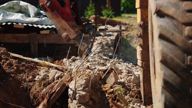 Close-up of a hydraulic breaker pressing twisted reinforcing steel into broken concrete foundation debris beside old wooden formwork during residential demolition and site cleanup.