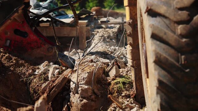 Heavy machinery with a hydraulic hammer attachment breaking apart a reinforced concrete foundation, creating dust and debris during the demolition process on a construction site