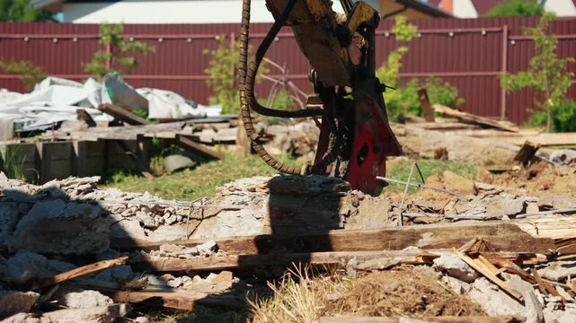 Powerful hydraulic breaker attachment on a construction excavator demolishing a reinforced concrete foundation, creating dust and rubble during the destruction process on a bright sunny day