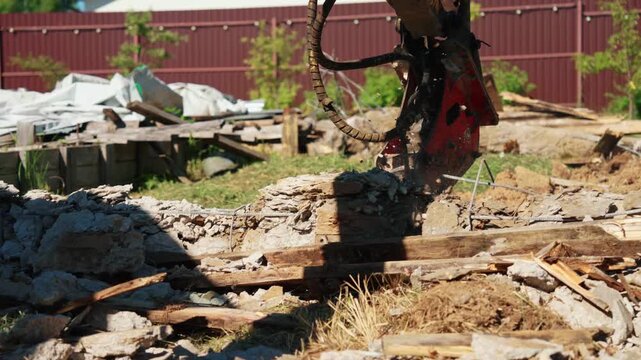 Low angle close-up of a hydraulic breaker hovering above broken concrete, wooden formwork and foundation debris during residential demolition, showing heavy equipment and site preparation.