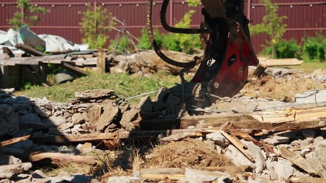Powerful hydraulic shears on an excavator arm demolishing reinforced concrete structures. Heavy machinery at work crushing stone and metal rebar during building demolition or reconstruction
