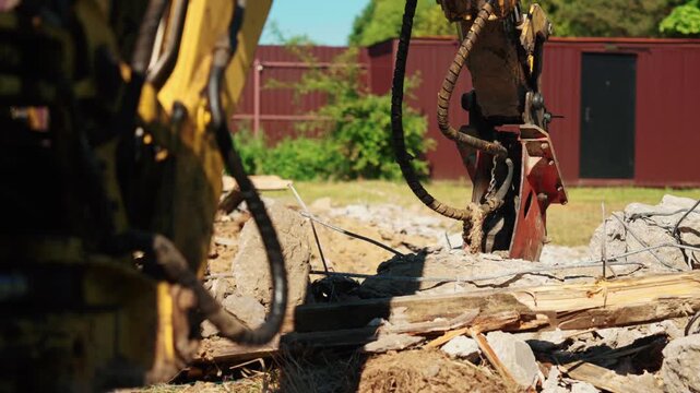 Heavy machinery with a hydraulic hammer attachment breaking reinforced concrete rubble during a building demolition project, dismantling an old foundation and creating debris on a sunny day