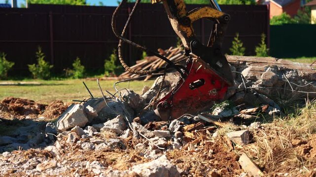 Low angle close-up of a hydraulic breaker resting on broken concrete rubble with twisted reinforcing steel and wooden debris during residential foundation demolition and site cleanup.