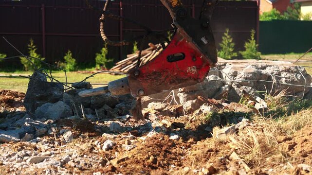 Professional heavy machinery with a hydraulic hammer attachment breaking reinforced concrete and stone during demolition work on a construction site, creating dust and rubble in the process