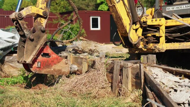 Heavy machinery with a hydraulic hammer attachment dismantling an old wooden retaining wall at a construction site, preparing the ground for new development and foundation work