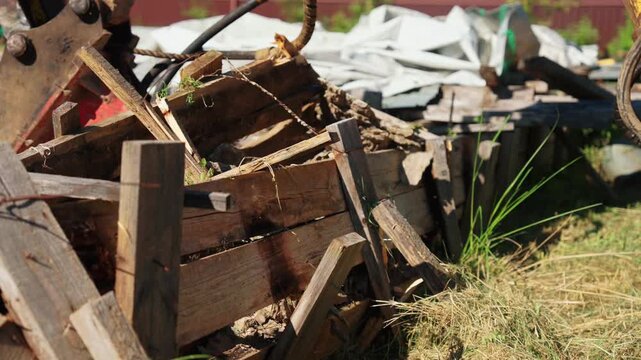 Discarded wooden beams, planks, and construction materials piled up in a grassy area outdoors. Messy heap of rubble and timber junk from a renovation or demolition project on a sunny day