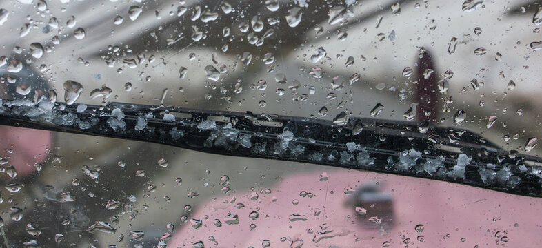 Black windshield wiper blade of pink vehicle coated with chunks of fallen hail and icy slush
