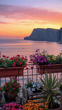 Beautiful balcony terrace with colorful potted flowers overlooking the sea and coastal cliffs at sunset