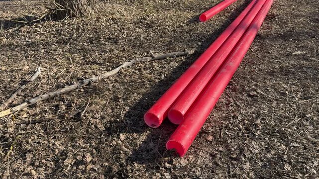 Red plastic pipes on soil, sunlit spring day, three pvc hot water tubes lying on gravel ready for replacement closeup view reveals