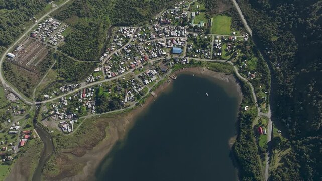 Aerial top-down perspective of the village of Puyuhuapi, urban layout along the coast of the fiord, surrounded by lush green forests and winding roads in the Aysen region of Patagonia, Chile.