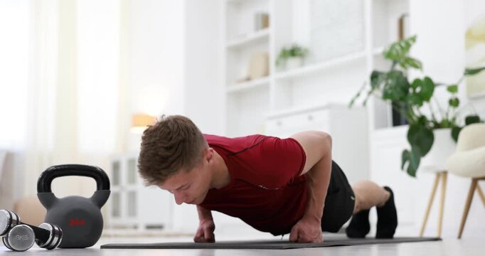 Athletic young man doing push ups on fitness mat at home