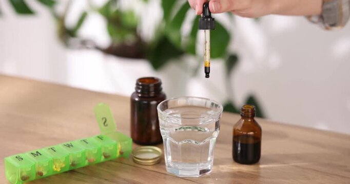 Woman dripping iodine into glass of water from pipette at wooden table, closeup