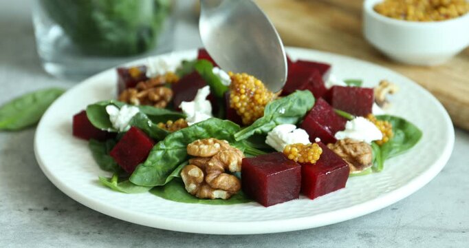 Adding mustard to salad with boiled beets at grey table, closeup