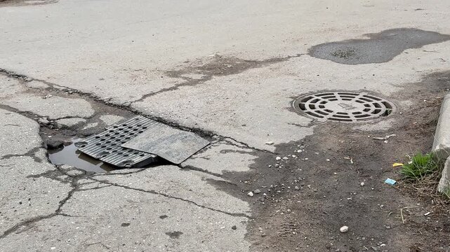 Large pothole on asphalt road covered with improvised metal plate, cracked pavement radiating fractures, shallow water pooling