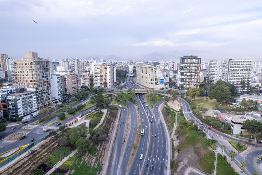 Aerial view of the Costa Verde highway winding through the urban landscape with modern high-rise buildings, green slopes, and traffic in Miraflores, Provincia de Lima, Peru.