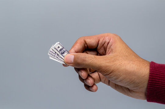 Close-up of a human hand holding tiny, miniature US dollar bills against a gray background. Inflation, low purchasing power, shrinking value of money, tight budgets, shrinkflation concept.