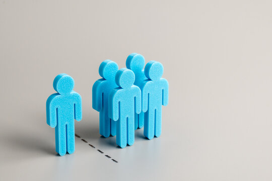 A group of blue human figures separated from a single individual figure on a gray background. Exclusion, uniqueness, individuality, isolation, leadership, or social alienation concept.