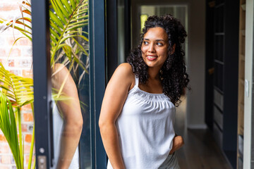 Fototapeta premium Adult African American woman leaning against glass door at home, wearing white blouse, palm visible