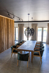 Naklejka premium Long table anchoring dining area with ten green chairs, black pendant lamps, curtains, glass doors