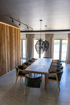Long table anchoring dining area with ten green chairs, black pendant lamps, curtains, glass doors
