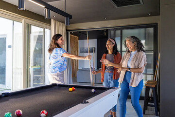 Naklejka premium Diverse female friends playing pool, holding cues in home game room with black felt table