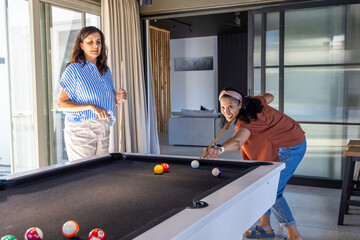 Naklejka premium Diverse women playing pool, lining up shots at home recreation area with black-felt table and cues