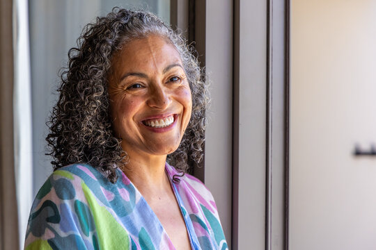 Senior African American woman standing smiling near window mullions wearing pastel print robe