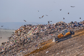 Bulldozer working at a landfill filled with household waste, garbage dump, environmental pollution, waste management, recycling and growing waste crisis © Vladimir Razgulyaev