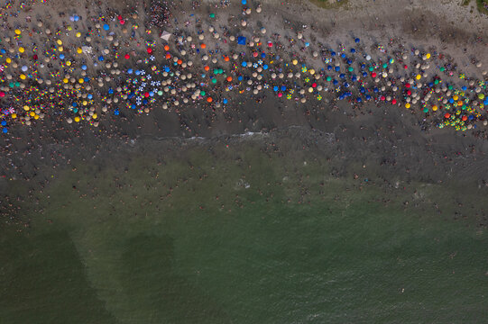Aerial view of Circuito de Playas with numerous colorful umbrellas scattered across the sandy beach and people swimming in the ocean in Barranco, Provincia de Lima, Peru.