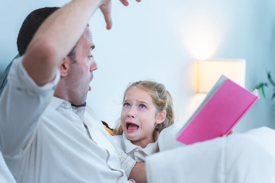 Father reading scary story to daughter, Dad and daughter bonding time reading a book together at home, Father reading a bedtime story to his daughter in bed