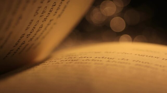 Cinematic video of a person flipping book pages printed with text under warm lamp light and blurry night bokeh