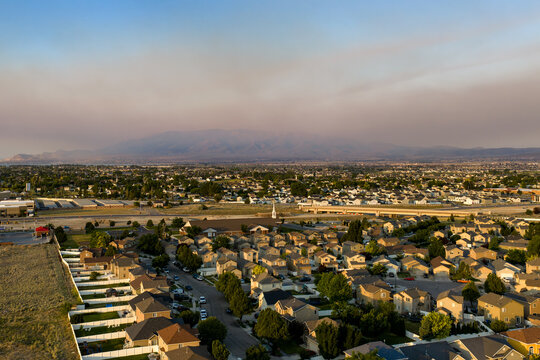 Aerial view of a suburban neighborhood with hazy skies from seasonal brushfires at sunrise, featuring rows of houses and distant mountains in Lehi, Utah, United States.