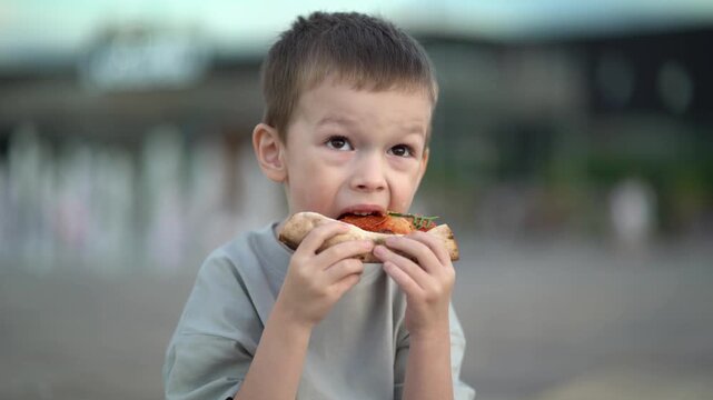 Young boy eats a messy snack with sauce on his face, making a funny expression. Cute candid childhood moment for family.