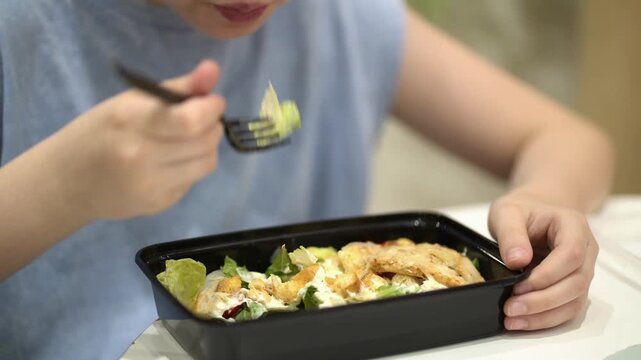Close-up of a child eating Caesar salad at a shopping mall food court, showcasing healthy nutrition and everyday family lifestyle.