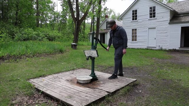 Man Operating Old Hand Water Pump in Historic Rural Village