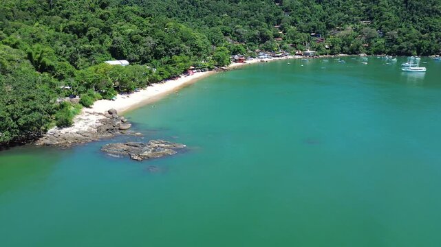 Sunny day aerial drone view of a massive rocky coastline with Picinguaba beach in the background, Ubatuba, Brazil.