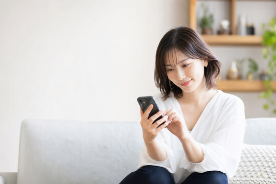 ソファでスマホを見る笑顔の日本人女性 Generative AI