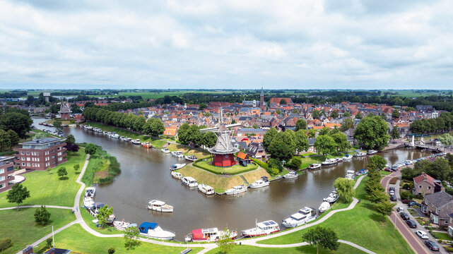 Aerial view of the historic windmill De Zuidermolen situated on a canal bank surrounded by moored boats, lush green lawns, and the charming townscape of Dokkum, Friesland, Netherlands.